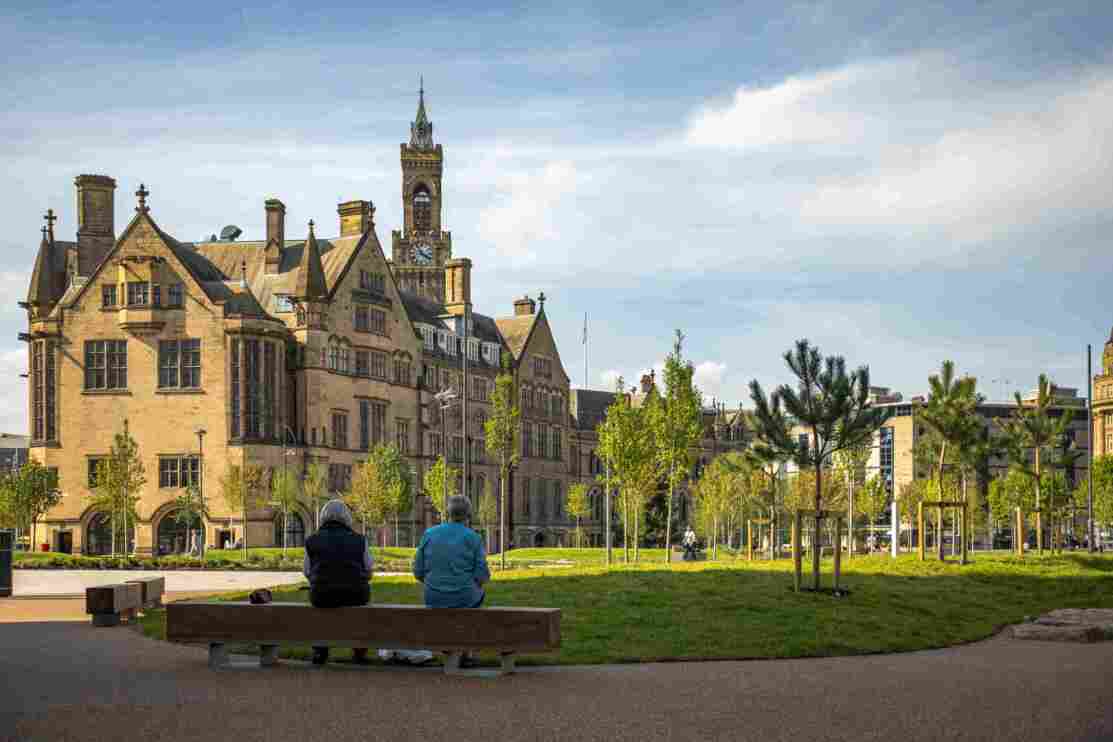 Two elderly people sitting on a bench in Norfolk Gardens, overlooking Bradford and Keighley Register Office.