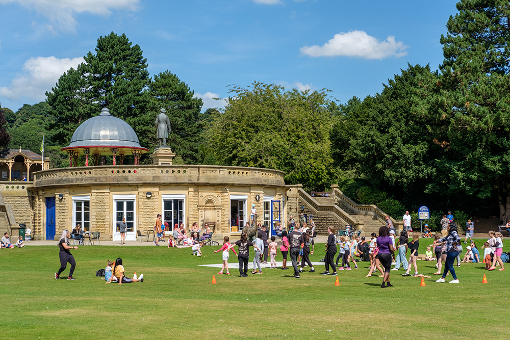 Photo of Roberts Park with children and adults playing on the grass, and people sitting at the café or relaxing on the lawn.